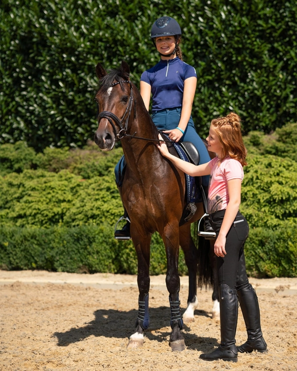 Bryczesy dziewczęce QHP Junior Lauren w kolorze petrol zaprezentowane przez modelkę podczas jazdy konnej