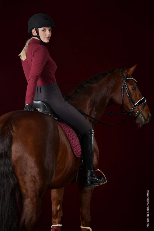 Koszulka jeździecka termiczna Schockemohle w kolorze cherry zaprezentowana przez modelkę podczas jazdy konnej