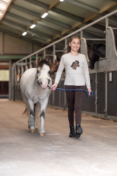 Bluzka jeździecka dziecięca HKM Junior z innymi akcesoriami z kolekcji Mia zaprezentowane przez modelkę
